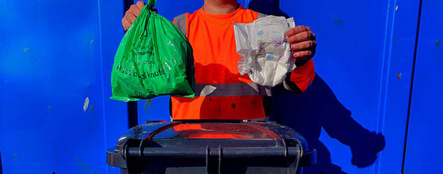 Kundeveileder holder opp en grønn matavfallspose og en bleie. Foto. 